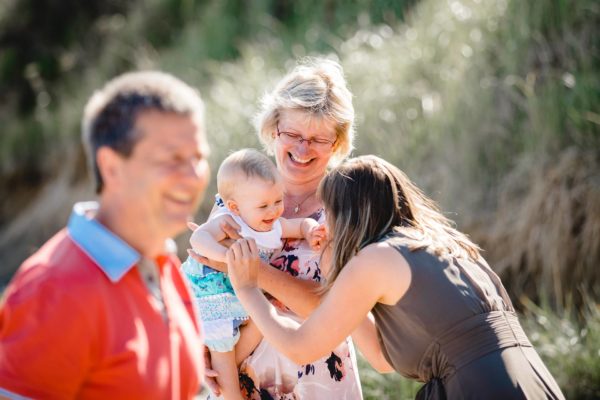 Oma-haelt-Baby-auf-dem-Arm-Mama-bringt-Baby-zum-lachen-Shooting-am-Strand-Familienfotografie-Fotograf-Rostock-Familienshooting