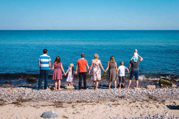 ganze-Familie-steht-Hand-in-Hand-direkt-am-Wasser-Ostsee-Shooting-am-Strand-Familienfotografie-Fotograf-Rostock - Familienshooting