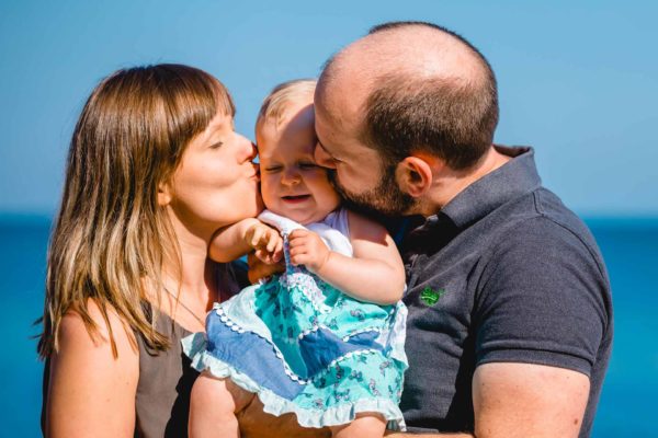 Mama-und-Papa-kuessen-Baby-gleichzeitig-auf-Wange-Shooting-am-Strand-Familienfotografie-Fotograf-Rostock - Familienshooting