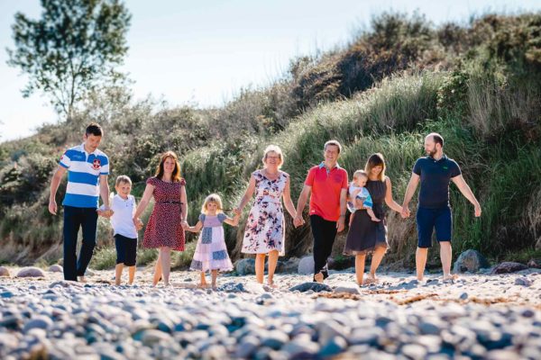 drei-Generationen-neun-Menschen-gehen-Hand-in-Hand-am-Strand-Shooting-am-Strand-Familienfotografie-Fotograf-Rostock-Familienshooting