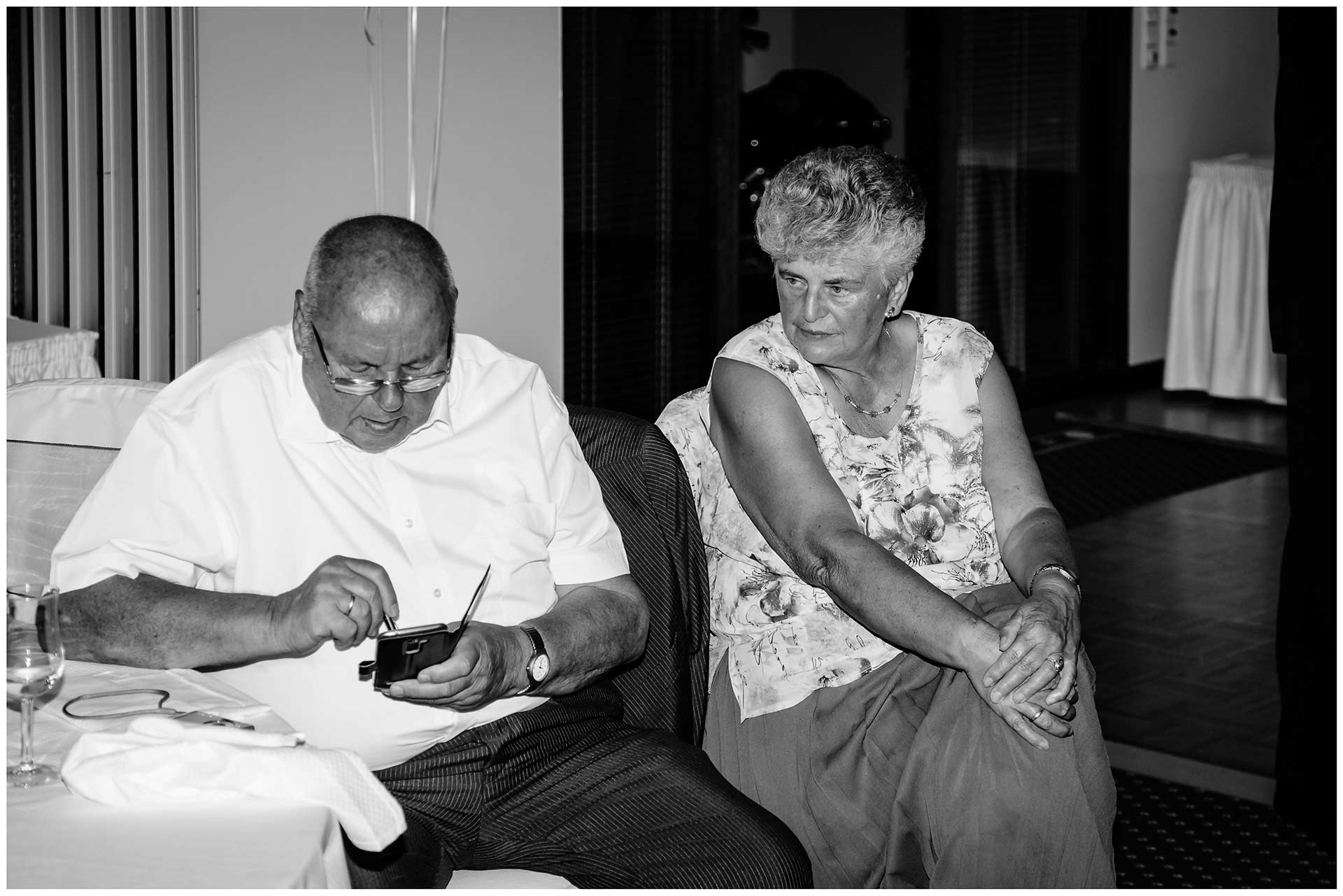 Hochzeitsgast-schaut-auf-sein-Handy-und-wird-von-seiner-Frau-dabei-beobachtet-Hochzeit-im-Hotel-Neptun-Hochzeitsfotograf-Warnemuende-Hochzeitsfotograf-Rostock-Hochzeitsfotograf-Ostseebad-Warnemuende