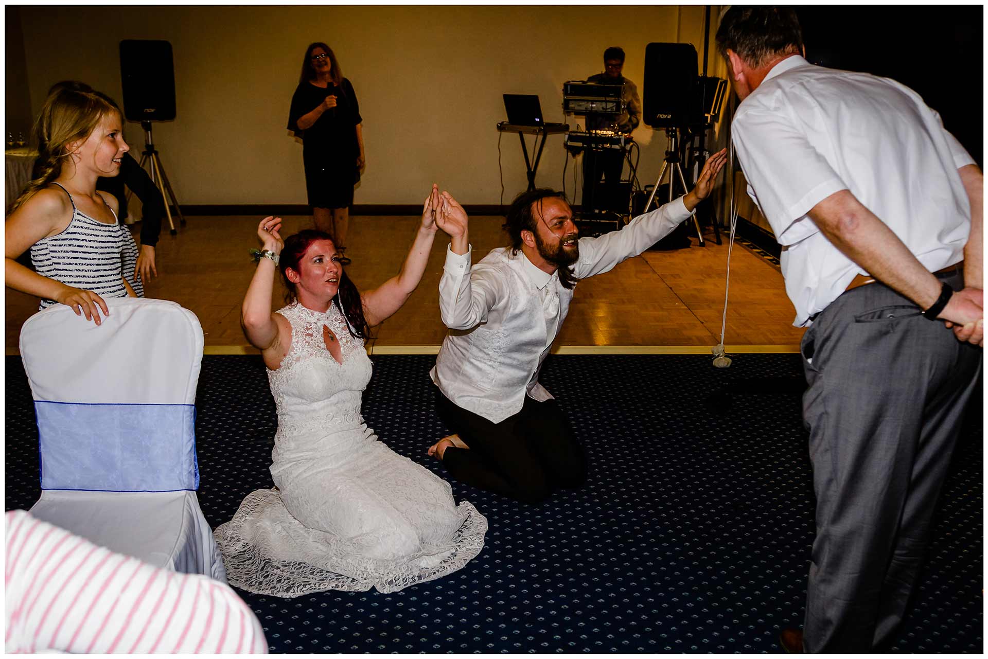 Brautpaar-kniet-auf-dem-Boden-und-beten-aus-Spass-den-Brautvater-an-Hochzeit-im-Hotel-Neptun-Hochzeitsfotograf-Warnemuende-Hochzeitsfotograf-Rostock-Hochzeitsfotograf-Ostseebad-Warnemuende