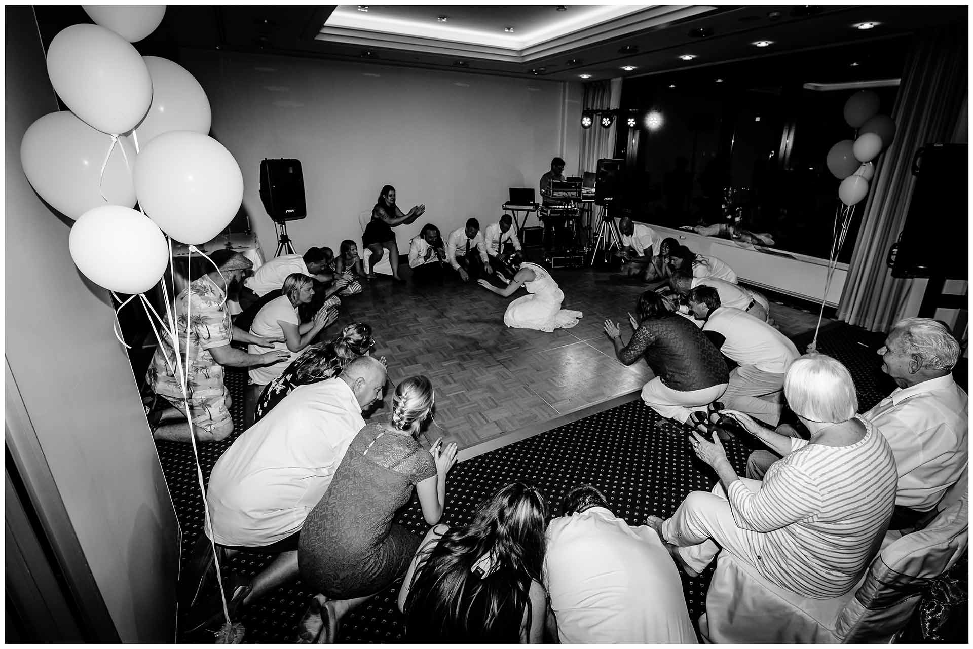 Brautpaar-und-Gaeste-knieen-auf-dem-Boden-We-will-rock-you-Queen-Hochzeit-im-Hotel-Neptun-Hochzeitsfotograf-Warnemuende-Hochzeitsfotograf-Rostock-Hochzeitsfotograf-Ostseebad-Warnemuende