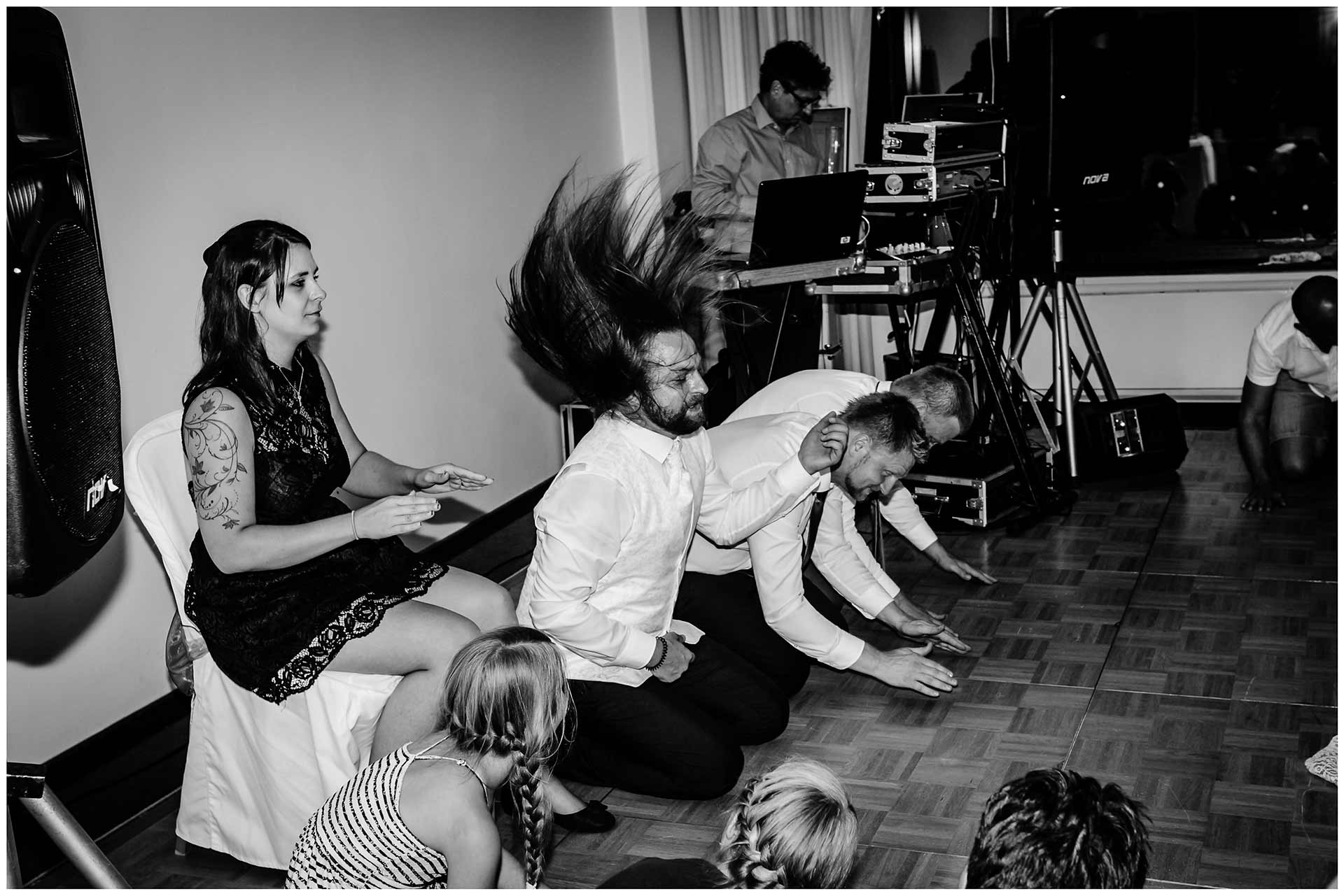 Brautpaar-und-Gaeste-knieen-auf-dem-Boden-We-will-rock-you-Queen-Hochzeit-im-Hotel-Neptun-Hochzeitsfotograf-Warnemuende-Hochzeitsfotograf-Rostock-Hochzeitsfotograf-Ostseebad-Warnemuende