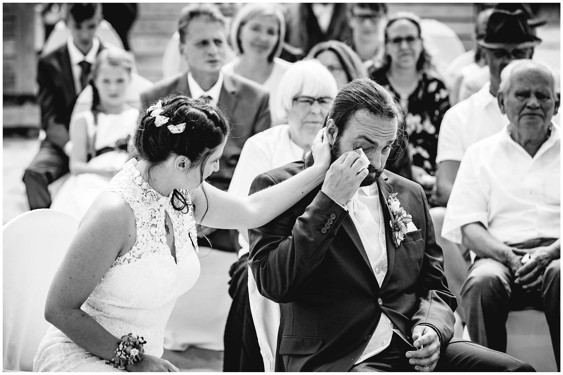 Braut-streichelt-liebevoll-die-Wange-ihres-Mannes_Braeutigam-wischt-sich-eine-Traene-aus-seinem-Gesicht-Hochzeit-am-Strand-Hochzeitsfotograf-Warnemuende-Hochzeitsfotograf-Rostock-Hochzeitsfotograf-Ostseebad-Warnemuende