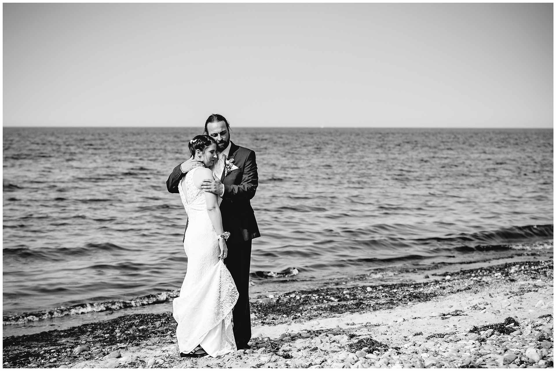 Hochzeitspaar-steht-Arm-in-Arm-mit-geschlossenen-Augen-am-Ostseestrand-Hochzeitsshooting-Hochzeit-am-Strand-Hochzeitsfotograf-Warnemuende-Hochzeitsfotograf-Rostock-Hochzeitsfotograf-Ostseebad-Warnemuende