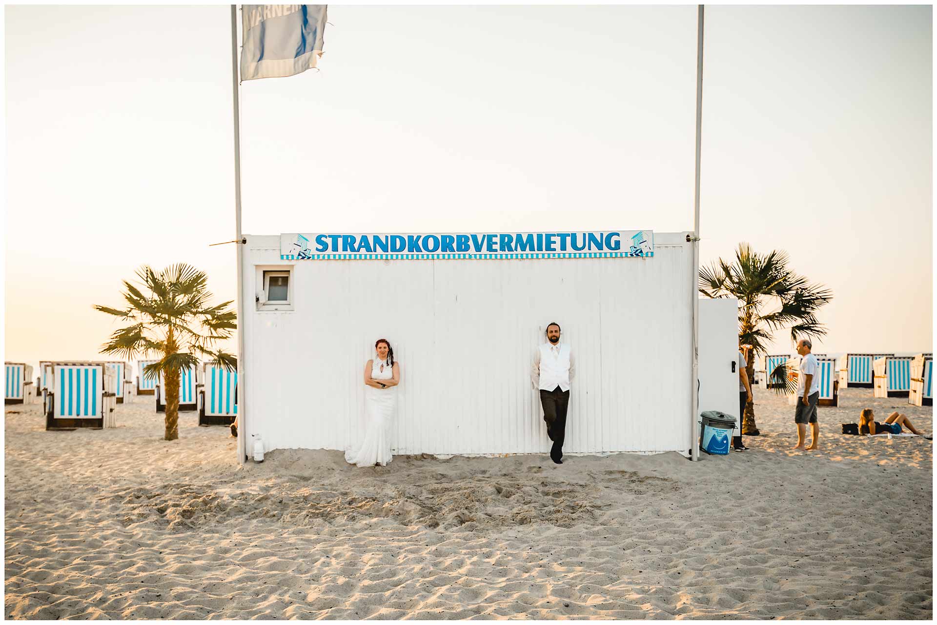 Brautpaar-steht-am-Haus-der-Strandkorbvermietung-Shooting-am-Strand-Hochzeitsfotografie-Hochzeitsfotograf-Warnemuende-Hochzeitsfotograf-Rostock-Hochzeitsfotograf-Ostseebad-Warnemuende