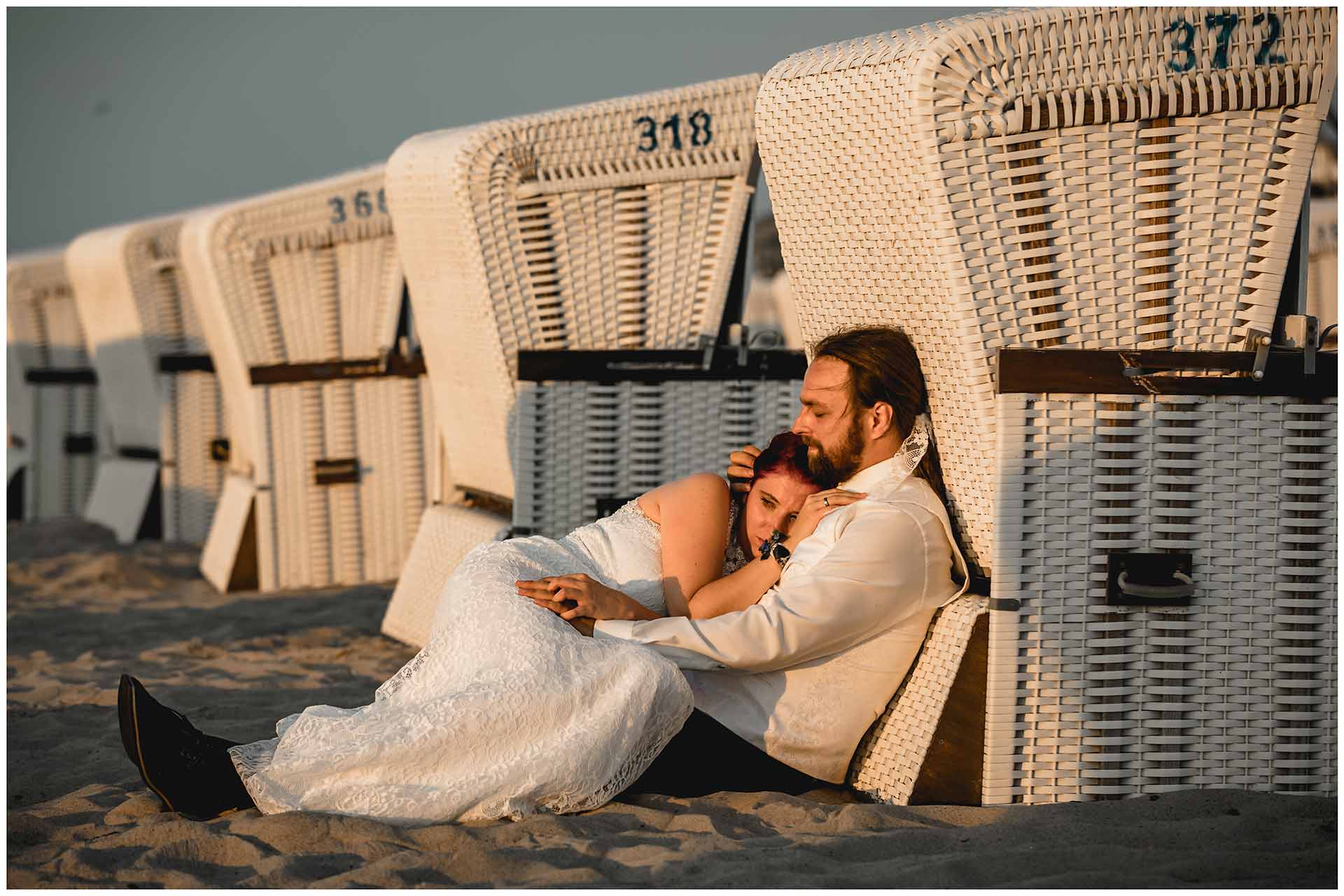 Braut-und-Braeutigam-liegen-eng-umschlungen-an-einen-Strandkorb-gelehnt-Hochzeitsfotografie-Hochzeitsfotograf-Warnemuende-Hochzeitsfotograf-Rostock-Hochzeitsfotograf-Ostseebad-Warnemuende