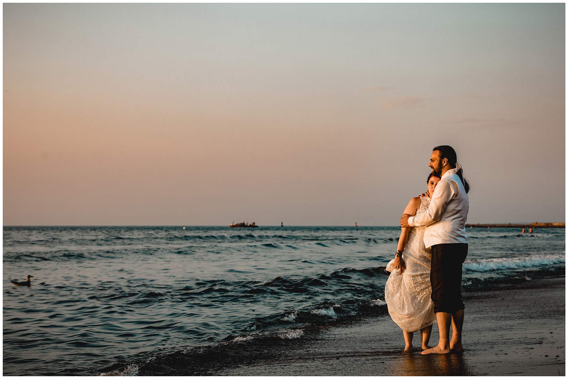 Brautpaar-steht-barfuss-und-arm-in-arm-direkt-an-der-Ostsee-Hochzeitsfotografie-Hochzeitsfotograf-Warnemuende-Hochzeitsfotograf-Rostock-Hochzeitsfotograf-Ostseebad-Warnemuende