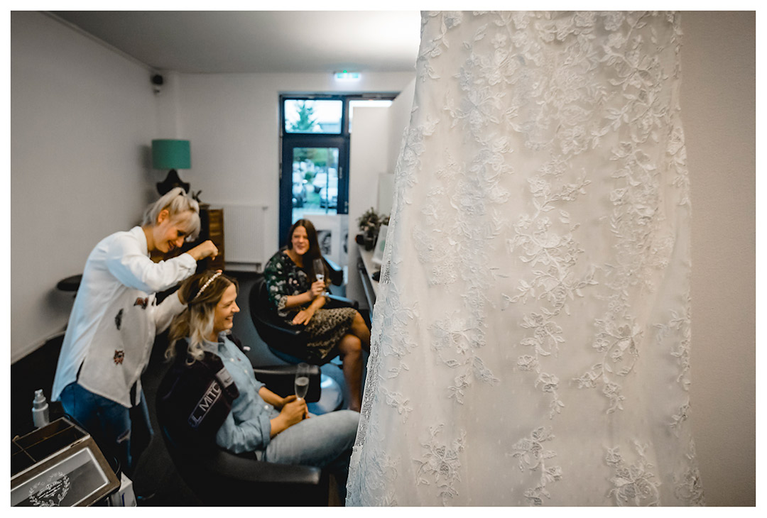 Vordergrund-Detailaufnahme-Hochzeitskleid-Hintergrund-Braut-Friseurun-Schwester - Fotograf Rostock