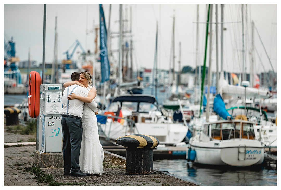 Brautpaar eng umarmt-im Hintergrund Segelboote - Stadhafen - Warnowufer - Hochzeitsfotos