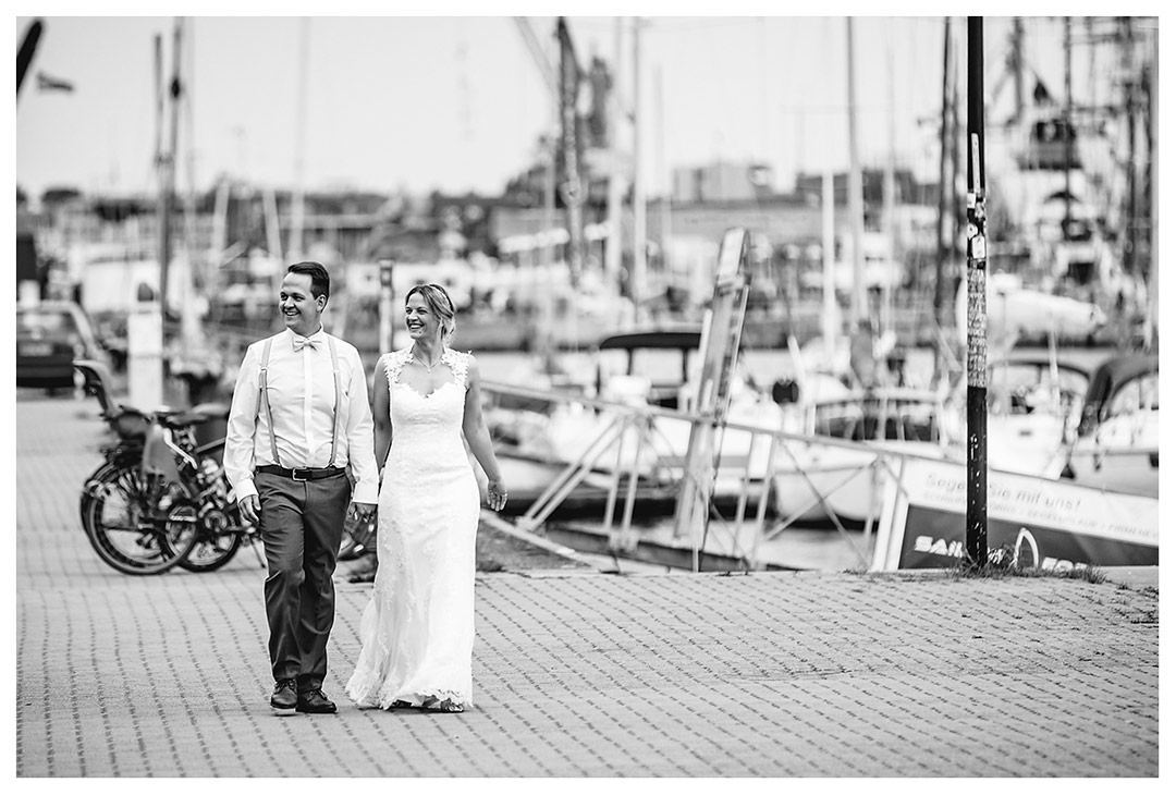 Hochzeitsfotograf Rostock - Brautpaar geht lächelnd Hand in Hand - Stadthafen - Warnowufer - Hochzeitsfotos