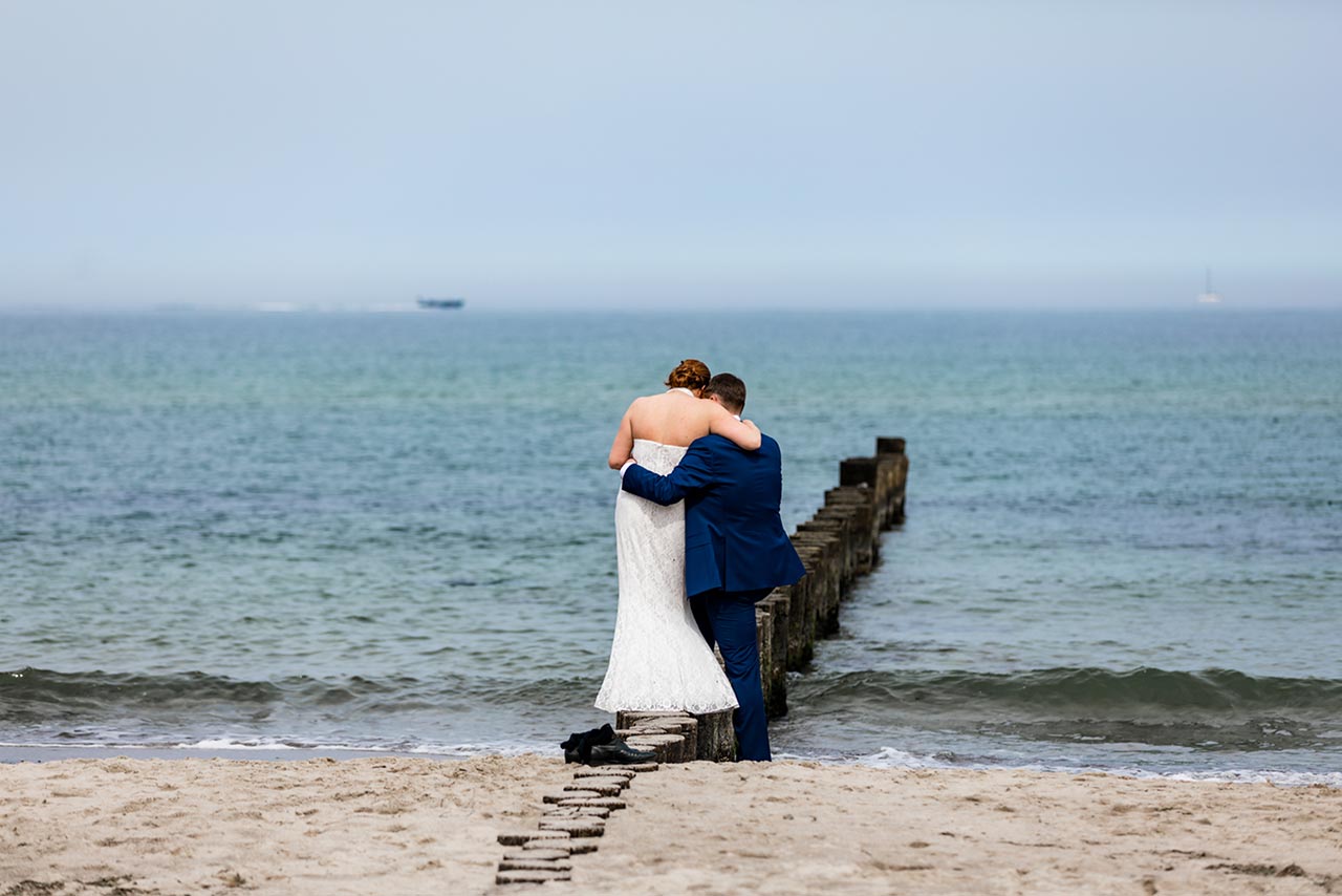 Brautpaar steht eng zusammen direkt am Wasser der Ostsee - Hochzeitsfotos - Fotograf Rostock Hochzeit