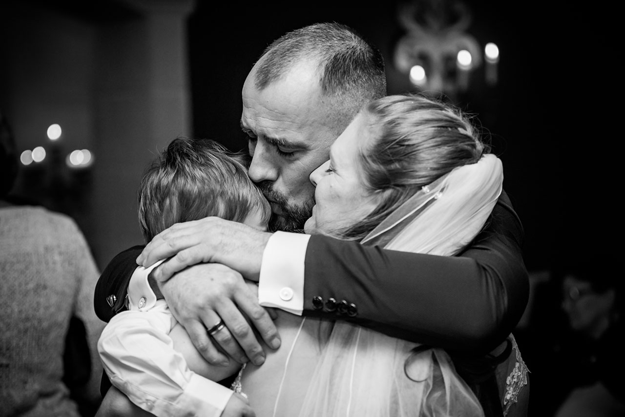 Brautpaar umarmt zusammen ihren kleinen Sohn - Bräutigam küsst kleinen Sohn auf die Stirn - Hochzeitsfotograf Bredenfelde