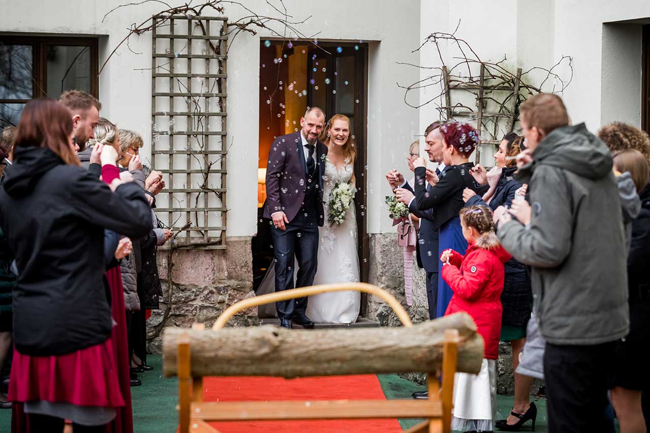 Hochzeitspaar kommt aus Tür im Vordergrund Baumstamm zum sägen - Hochzeitsfotograf