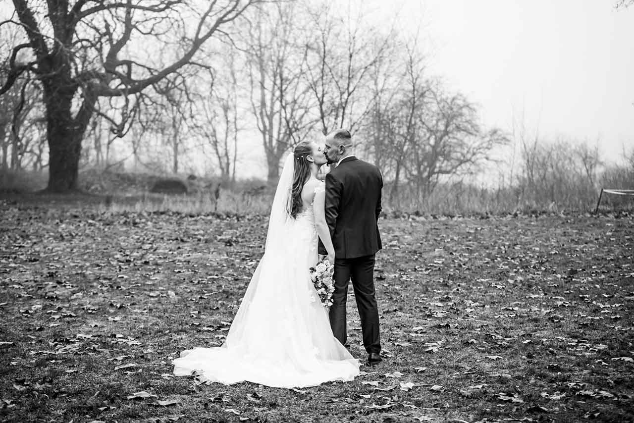 Brautpaar von hinten zu sehen küsst sich und steht auf Wiese - Hochzeitsshooting - Hochzeitsfotografie - Hochzeitsfotograf Bredenfelde