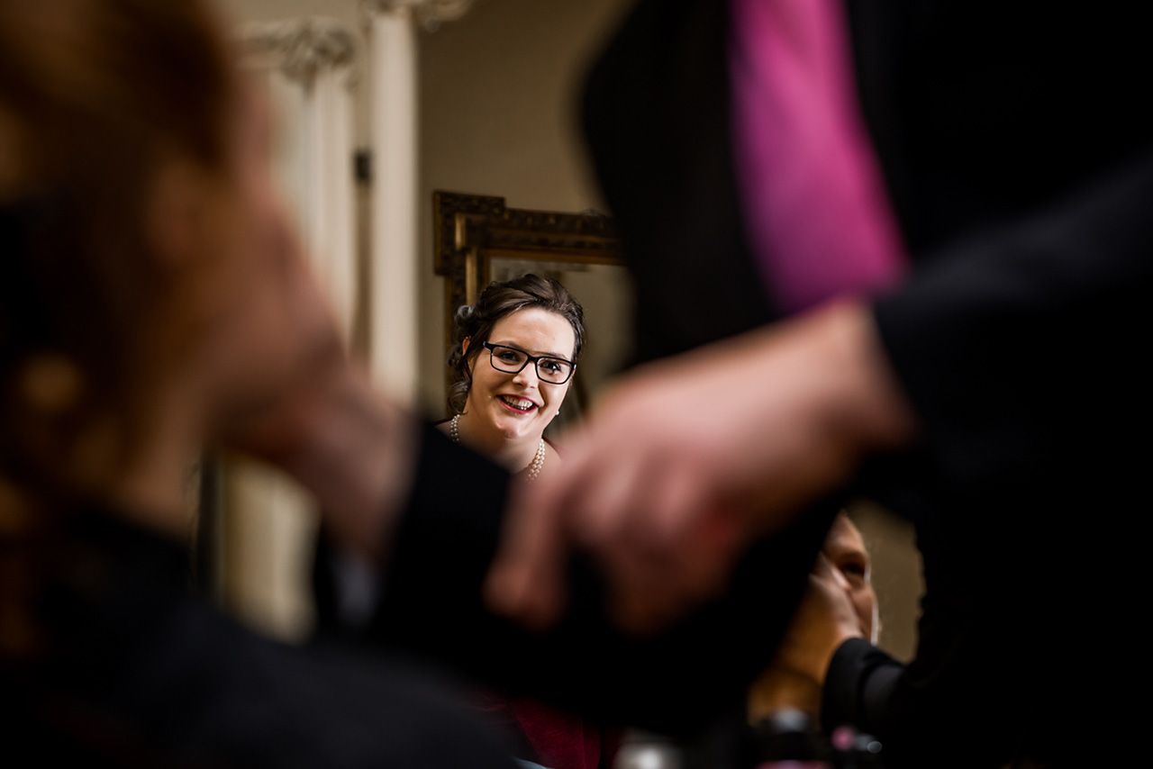 Freundin schaut beim Schminken der Braut zu und lächelt - Hochzeitsfotograf