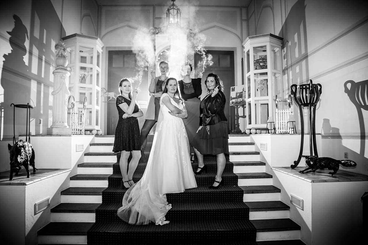 Gruppenfoto Braut steht cool ihren besten Freundinnen auf Treppe im Eingangsbereich Schloss Bredenfelde und alle rauchen - Hochzeitsfotograf Bredenfelde